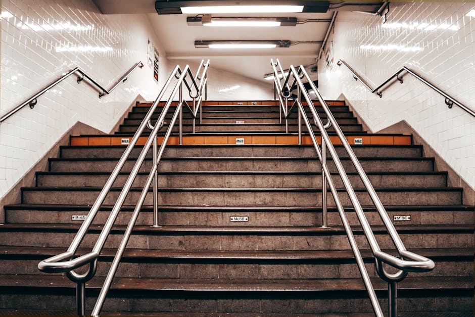 A set of escalators inside a building with a metal frame and black rubber steps, seen through an open doorway beneath a sign that reads 'The Crossing.' The space surrounding the escalators includes metallic walls and a small black mat on the floor at the entrance, indicating a station or transit point. The image highlights the interior environment where home relocation or moving services provided by Man With a Van New Cross may involve navigating stairs or access points during furniture transport or packing and moving processes, illustrating the logistical considerations of house removals within a busy urban setting.